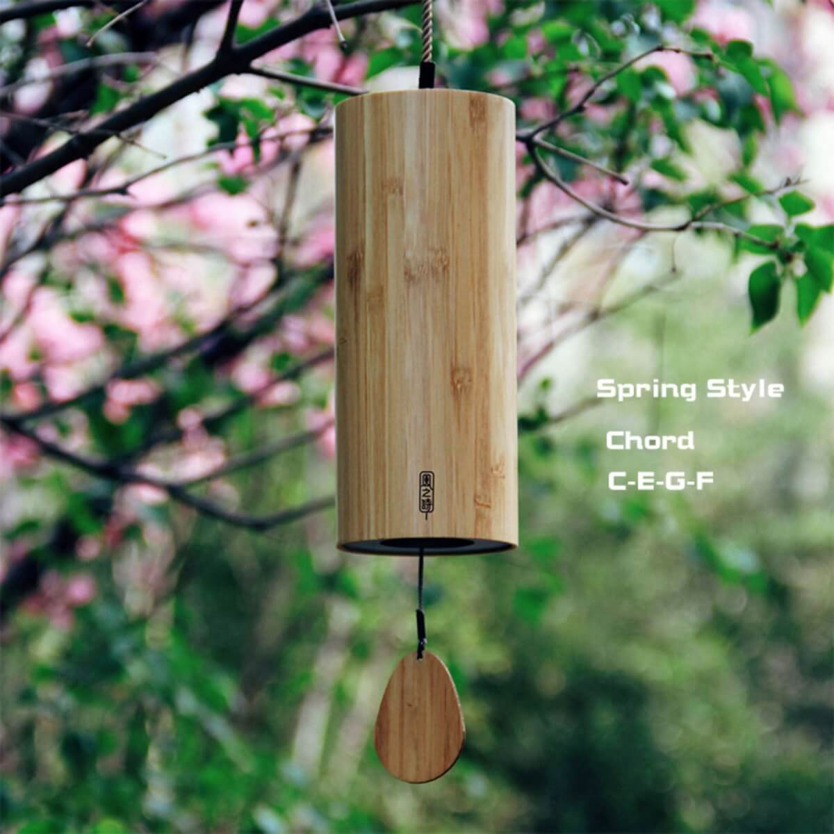 Bamboo wind chime with 4 melodies hanging outdoors among pink blossoms and green leaves.