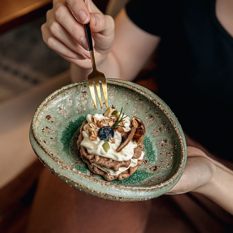 Artisan Green Dinnerware: Rustic stoneware bowl with textured glaze, holding a pastry.