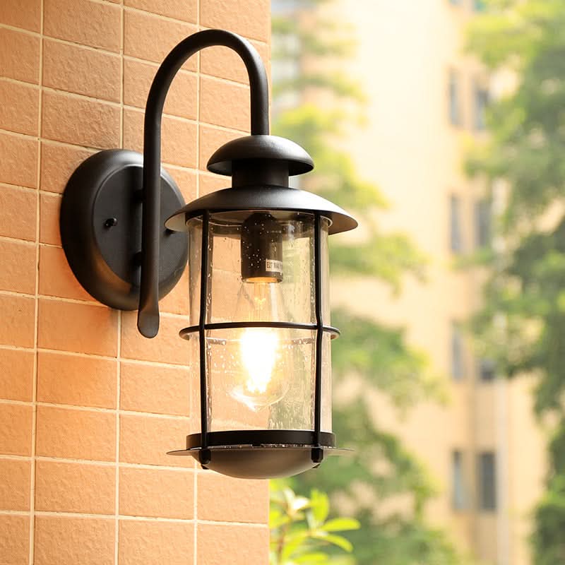 Black cylindrical outdoor sconce with clear glass shade, mounted on brick siding.