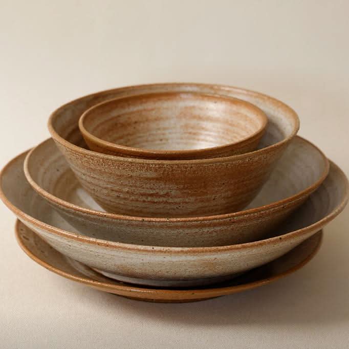 Brown clay tableware handmade set, rustic earthenware bowls and plates stacked on a neutral surface.