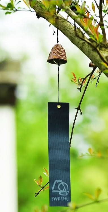 Japanese Pine Cone Wind Chime. Rustic bronze bell hanging from tree branch with dark striker.