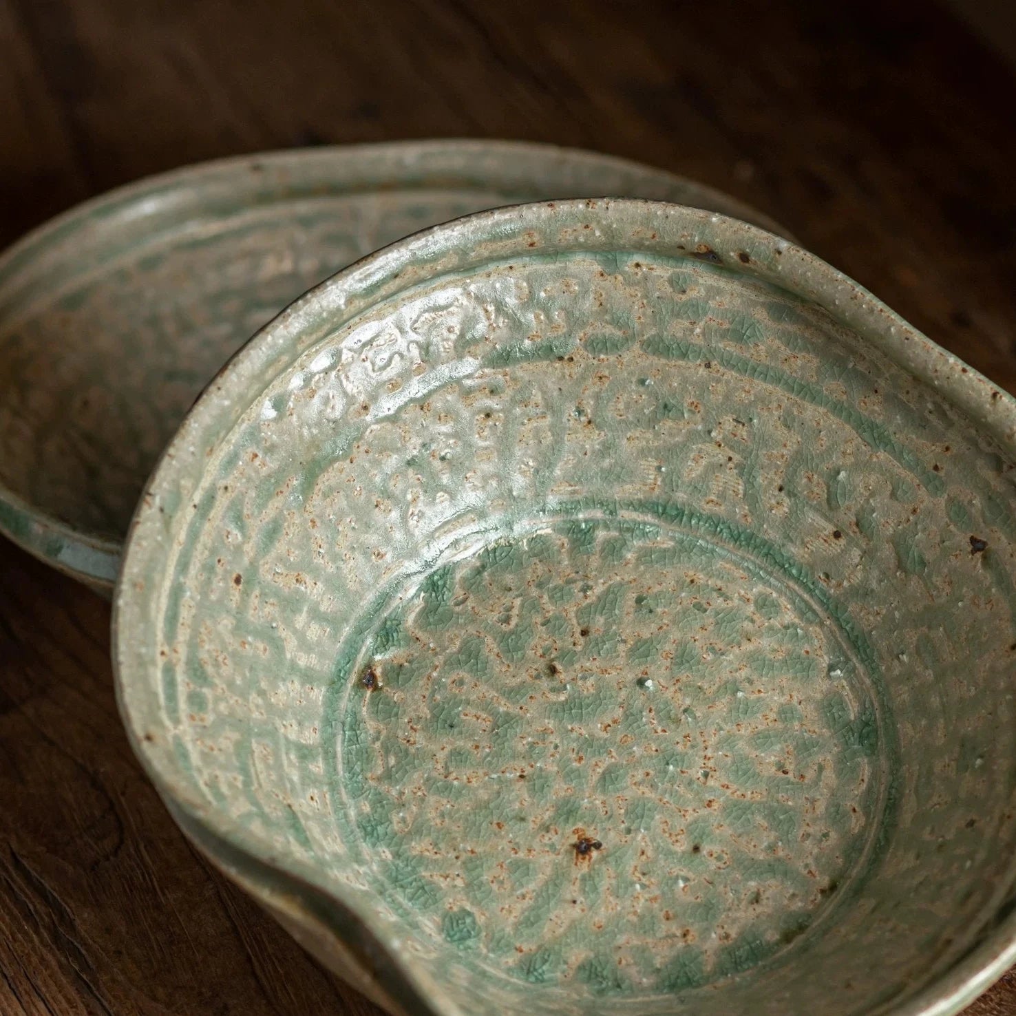 Close-up of a deep, wide ceramic bowl with a pouring lip and textured, speckled greenish-blue glaze.