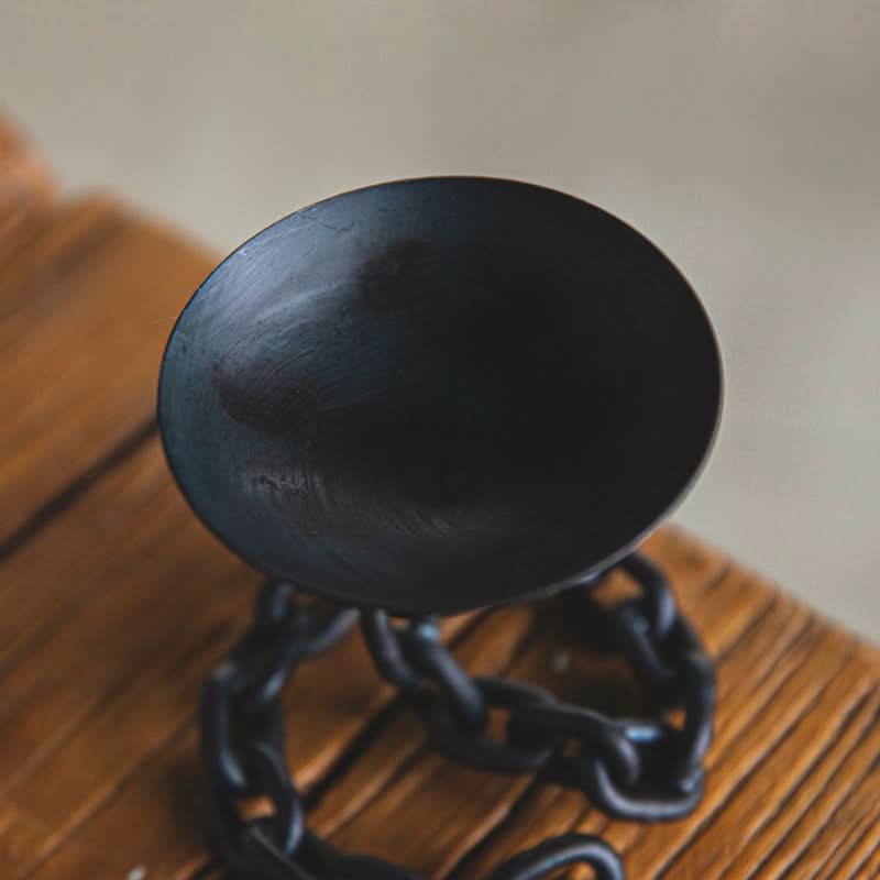 Black chain candle holder with a matte black bowl on a wooden surface.
