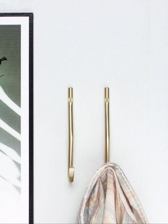 Minimalist brass wall hooks with a gold finish, holding a folded patterned cloth against a white wall.