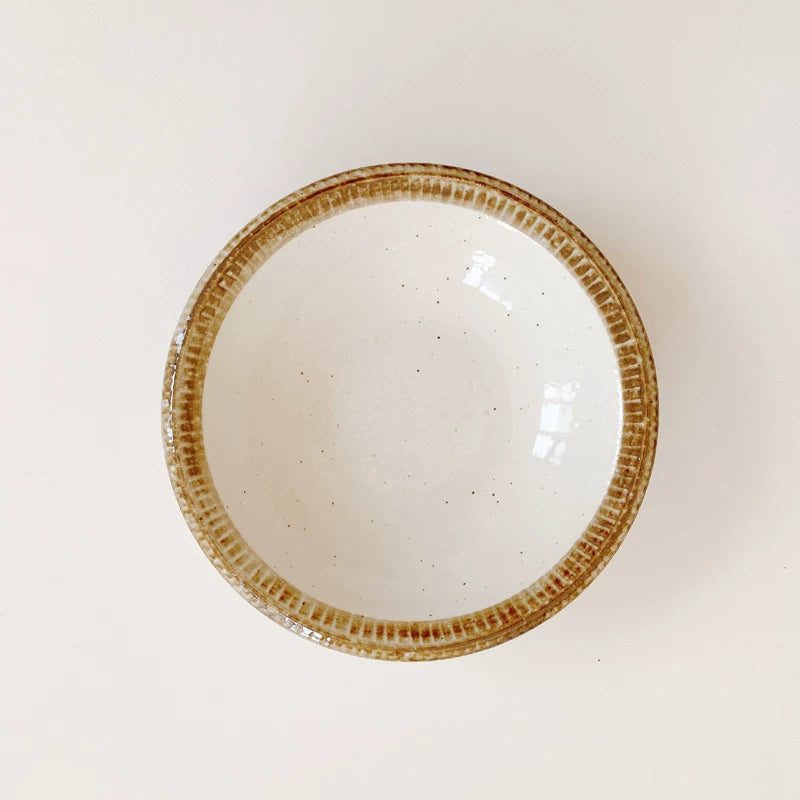Medium ceramic serving bowl shown from above, speckled white interior and textured brown rim.