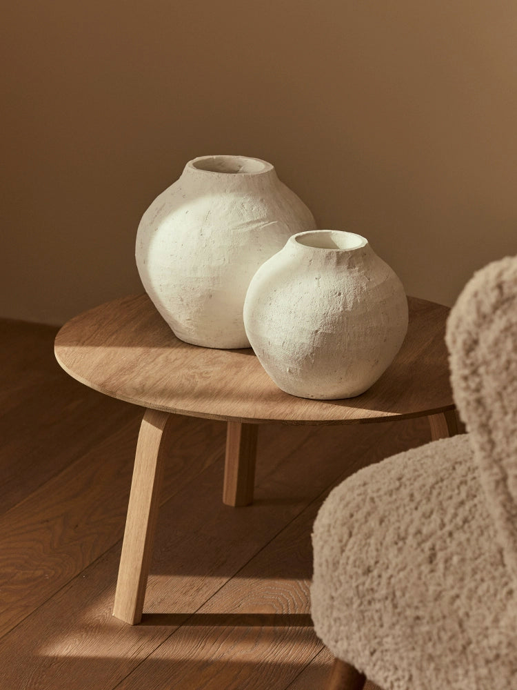 Two white ceramic vases, textured, on a light brown wooden coffee table. Boho style home decor.
