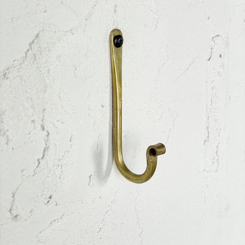 Gold J-shaped wall hook made of brass, mounted on a textured white wall.