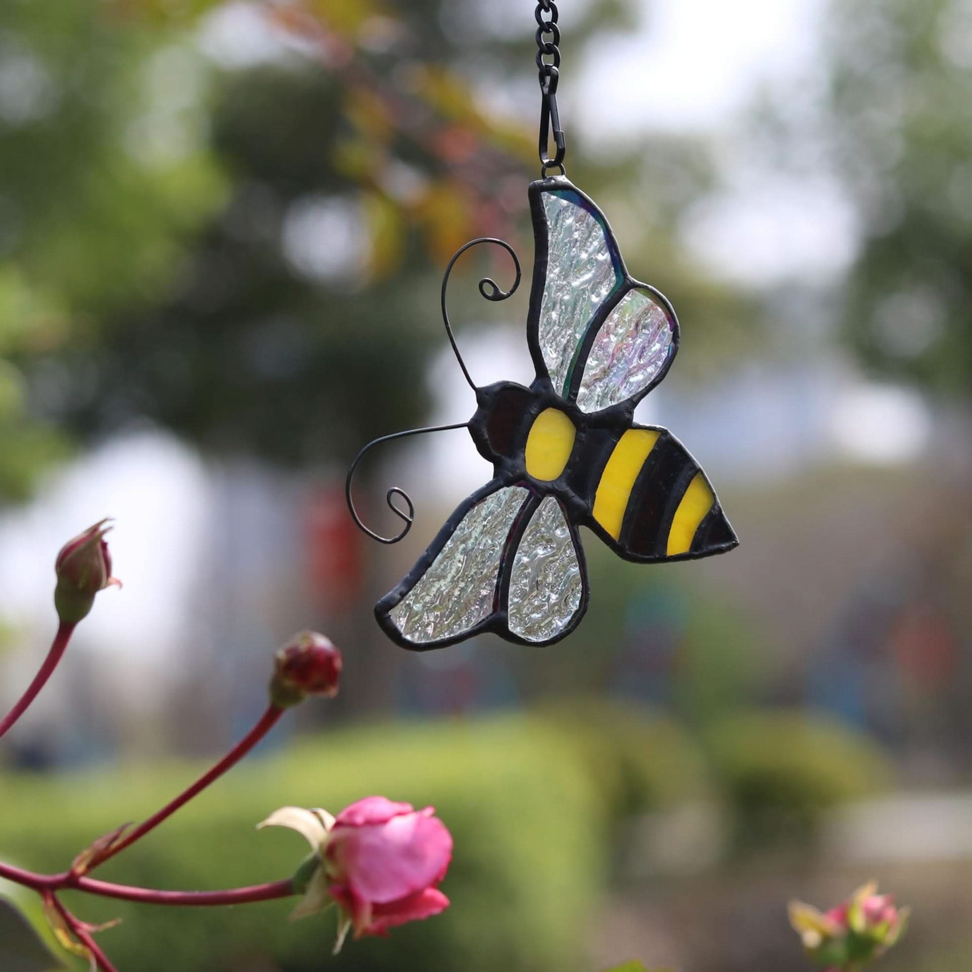 Stained glass bumblebee suncatcher with iridescent wings hanging outdoors near roses.