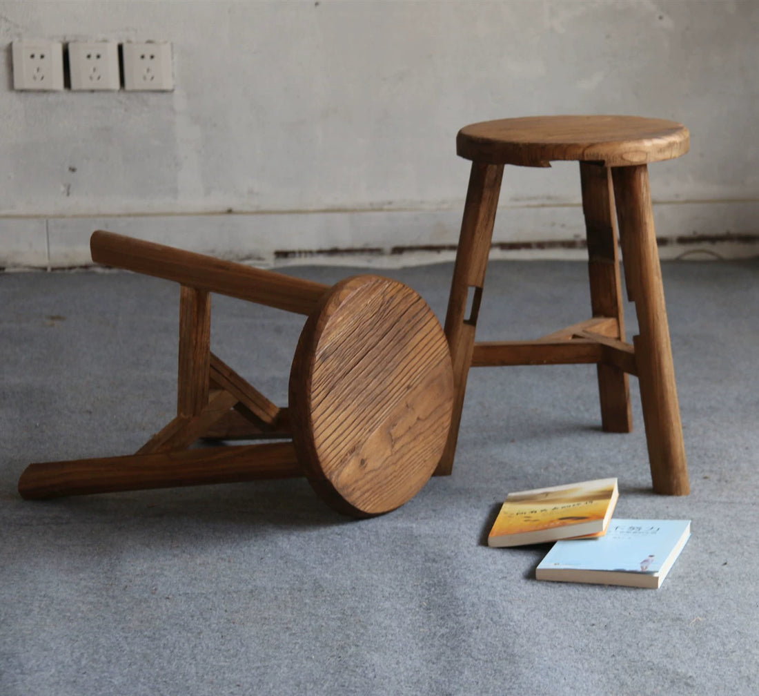 Rustic wooden stool, round top, natural wood finish, simple tripod base,  on gray carpet.