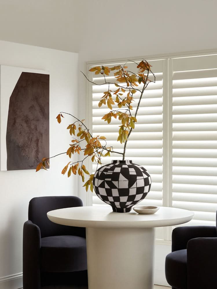Black and white checkered ceramic vase with autumn branches on a table.