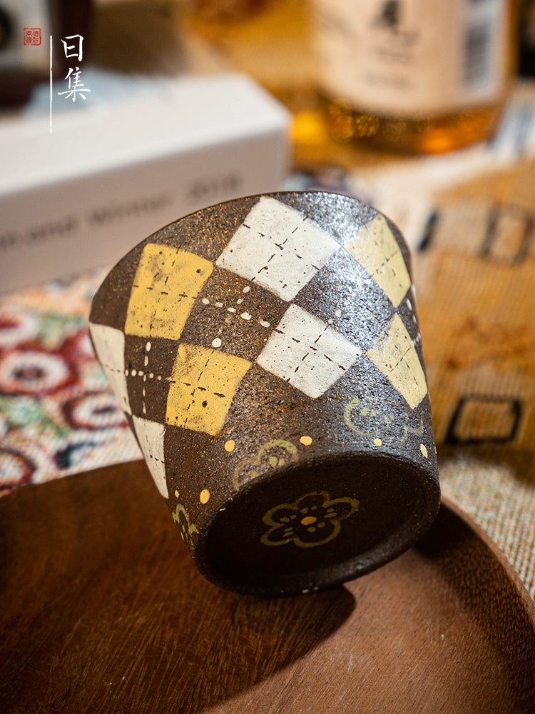 Hand-painted Japanese ceramic tea cup with diamond pattern, on a wooden saucer.
