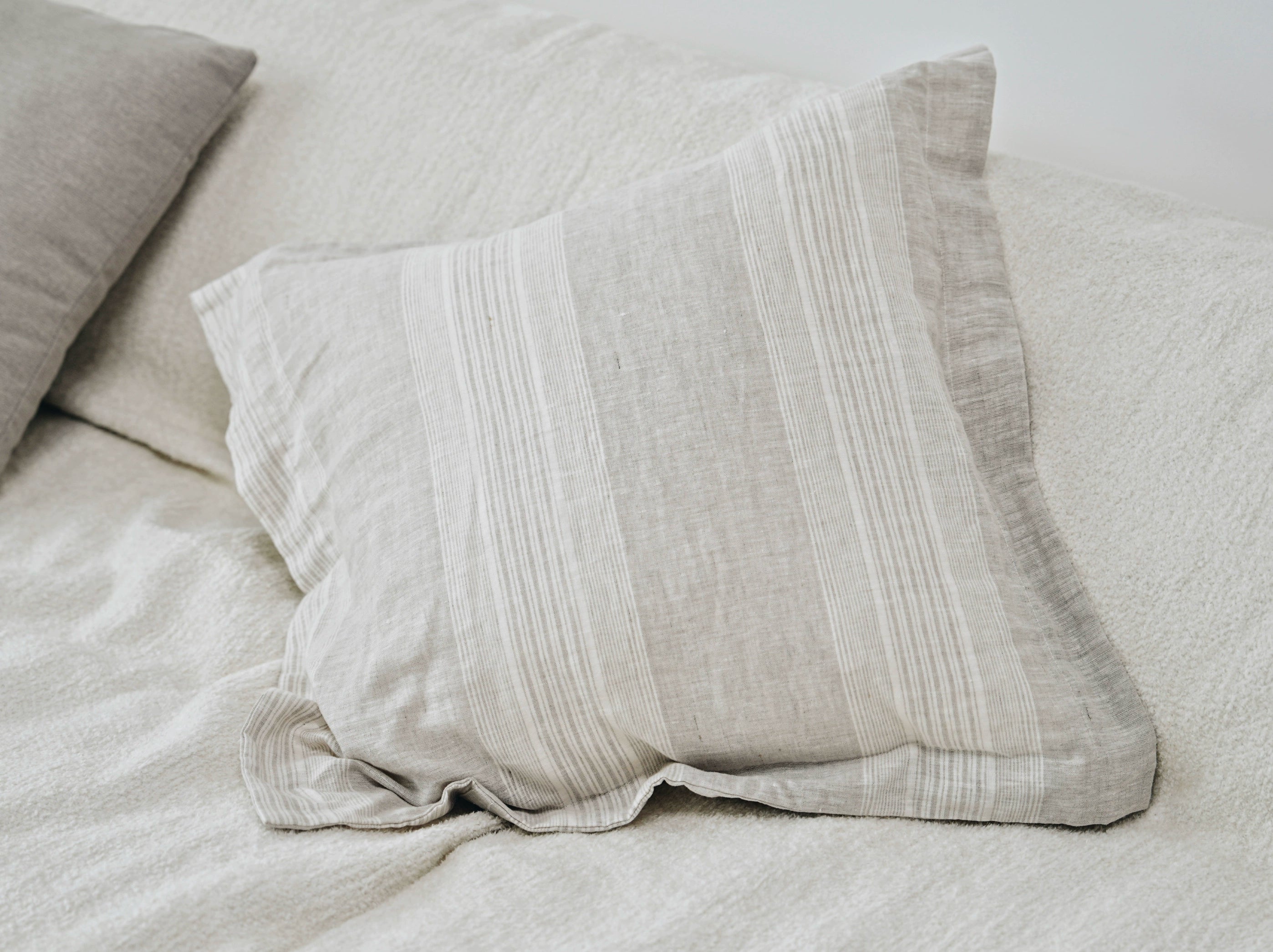Gray striped linen pillow cover on a textured cream sofa.