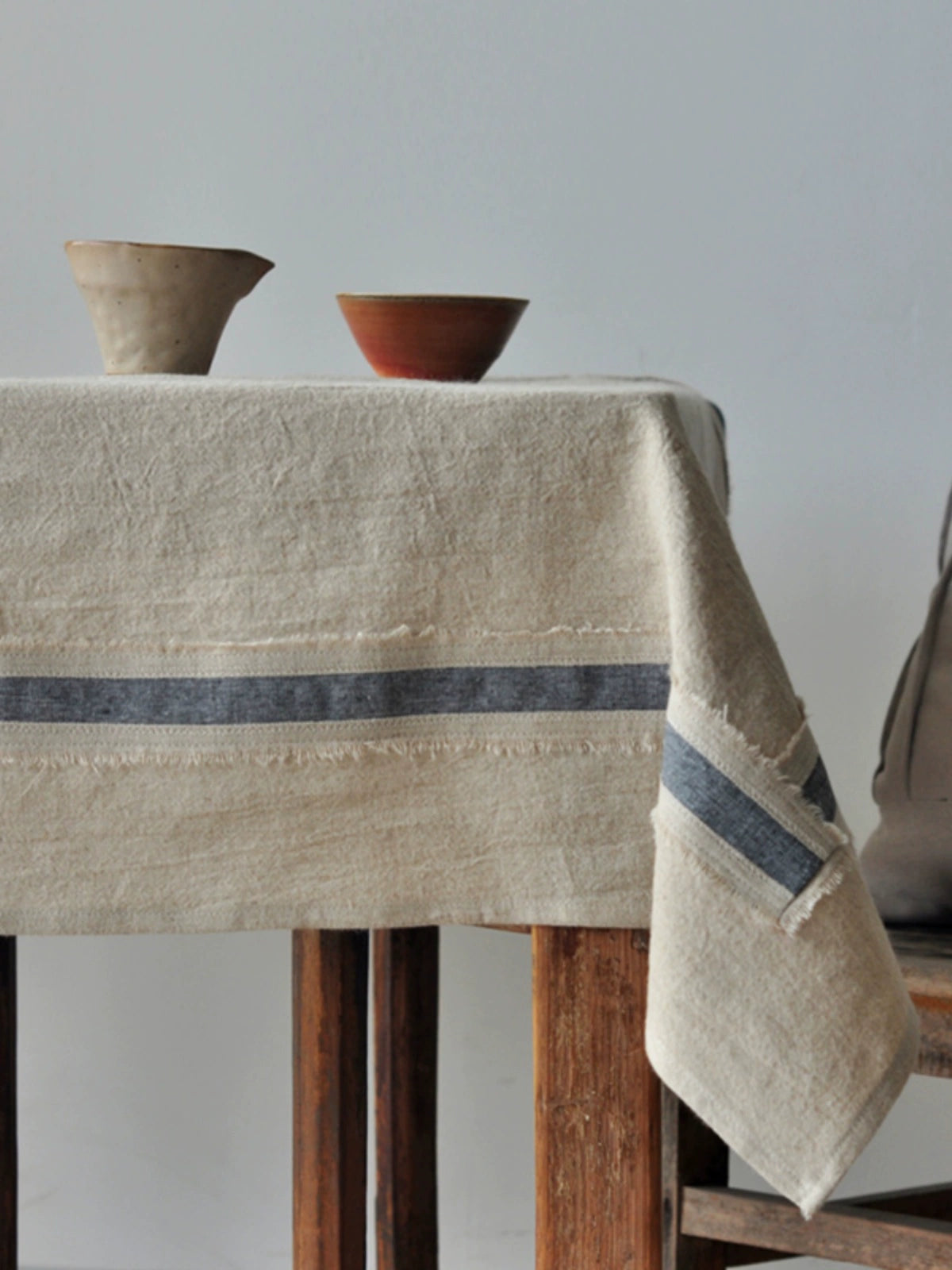 Rustic linen tablecloth with natural beige stripes, farmhouse style, draped over a wooden table with ceramic bowls.