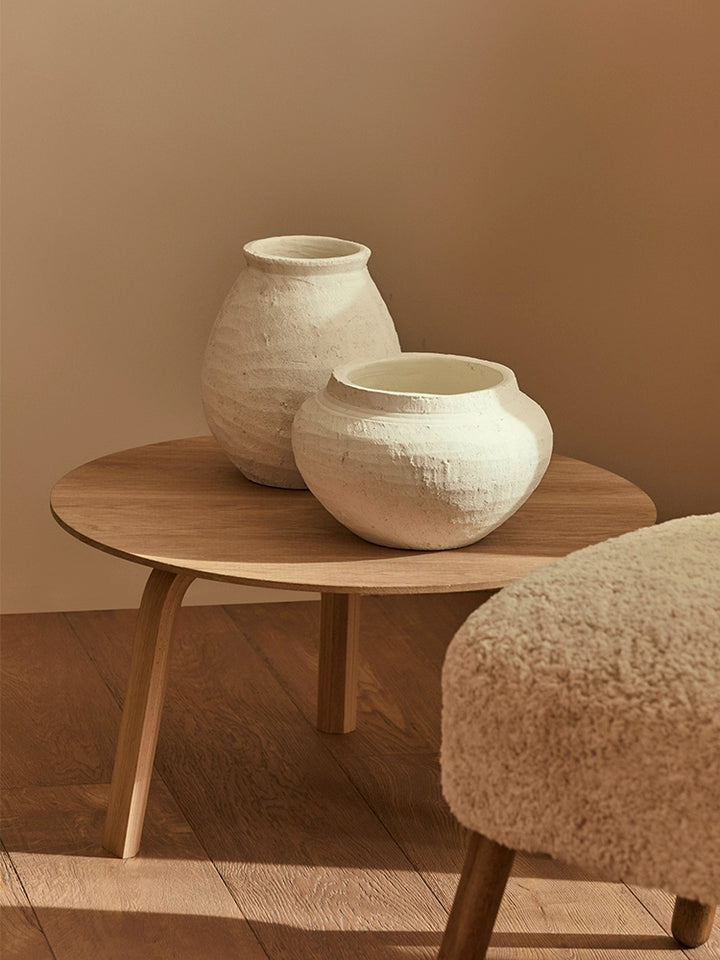 Two white ceramic vases, rustic style, on a light brown wooden coffee table.  Textured finish.