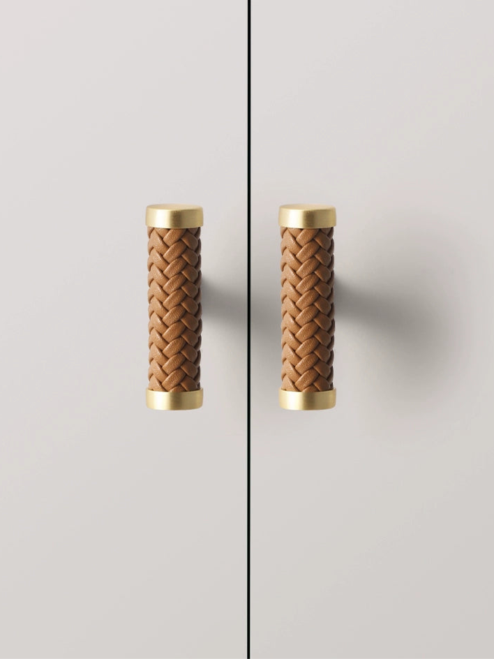 Two woven leather drawer pulls, light brown with gold accents, mounted on light gray cabinets.