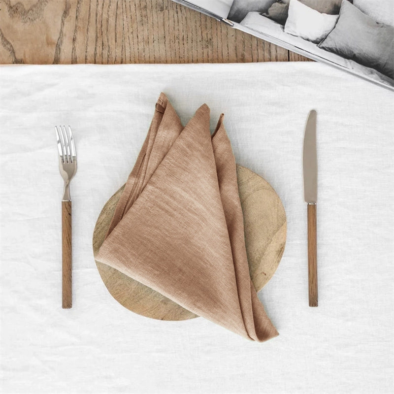 Elegant linen table napkins in taupe, knotted on a wood charger, set for four.