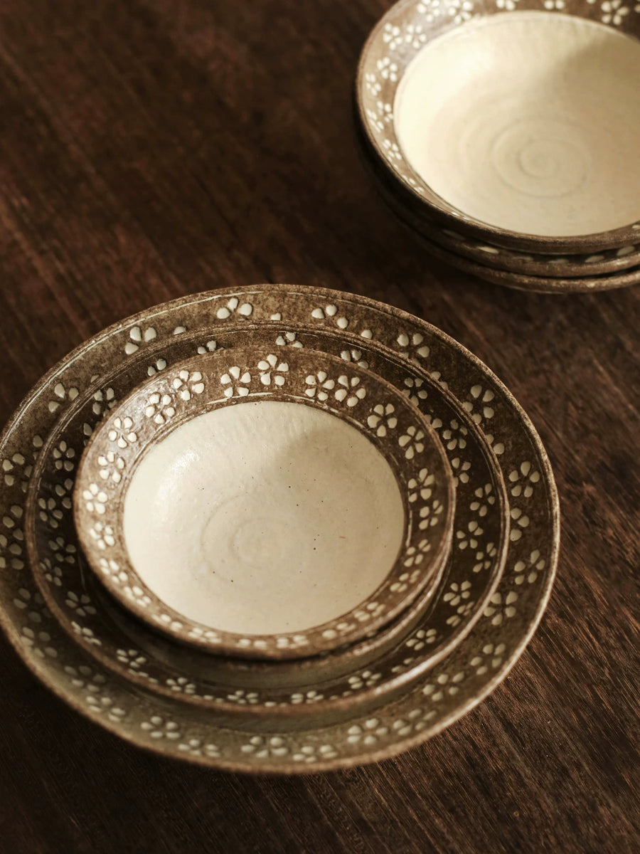Close-up of stacked ceramic bowls and plates with brown floral pattern on dark wood.
