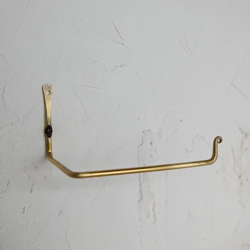 Gold toilet paper holder mounted on a textured white wall, brass material.