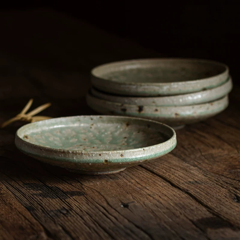 Stack of four rustic, handmade ceramic plates with a speckled green glaze on a dark wooden table.