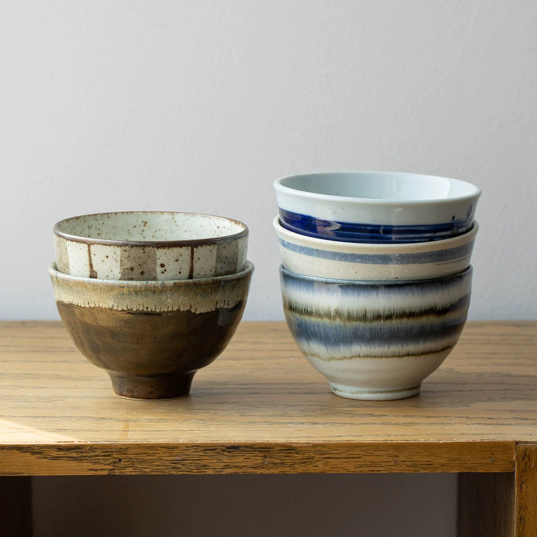 Stack of two brown speckled bowls and a stack of two blue-striped bowls on a wooden shelf.