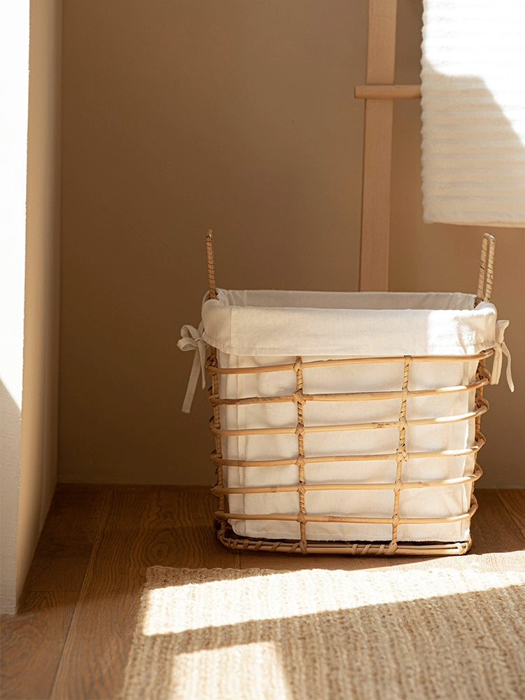 Light beige rattan laundry basket with removable white linen liner.  Stylish storage basket on a light brown floor.