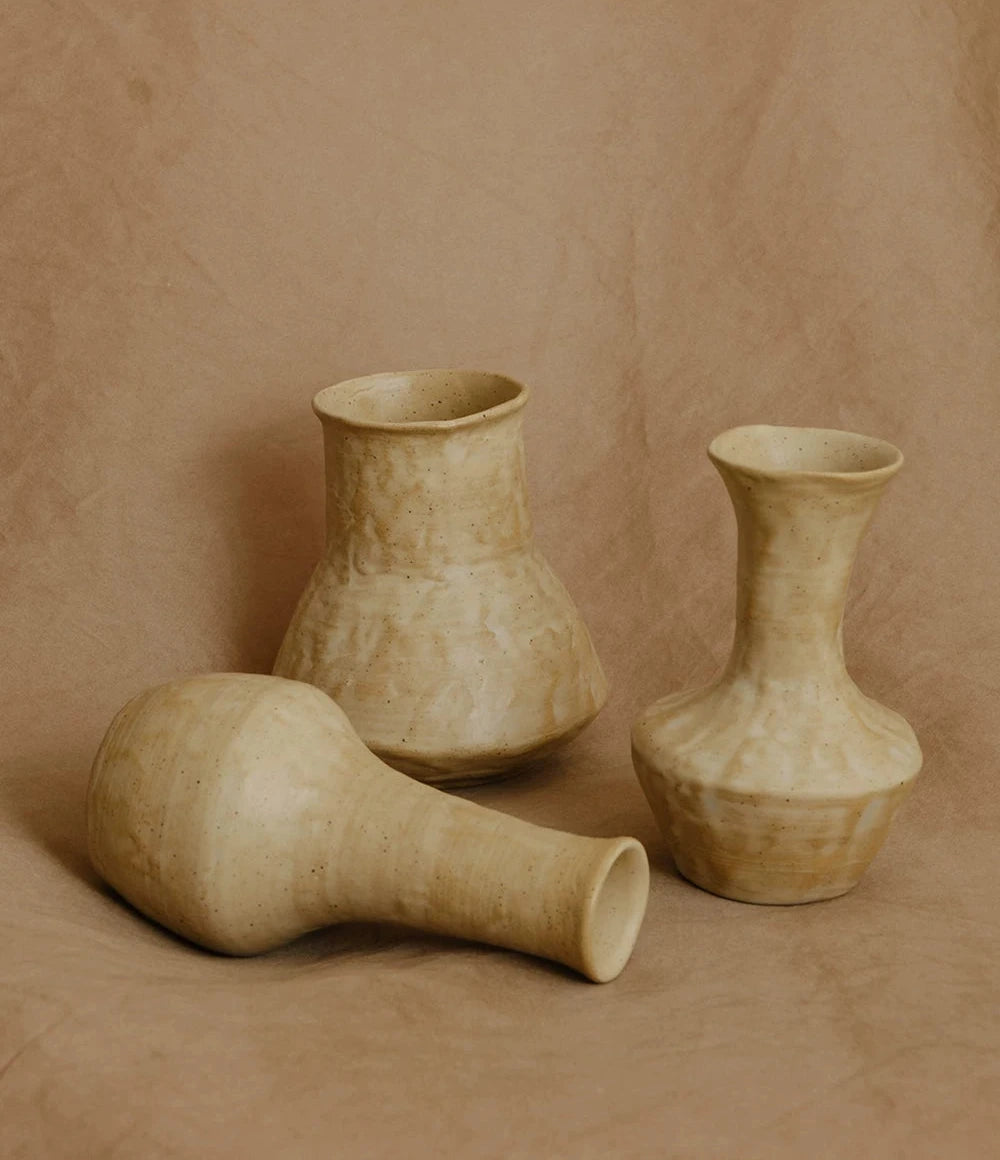 A small, hand-thrown ceramic vase with a textured, creamy white curd glaze and a narrow neck.