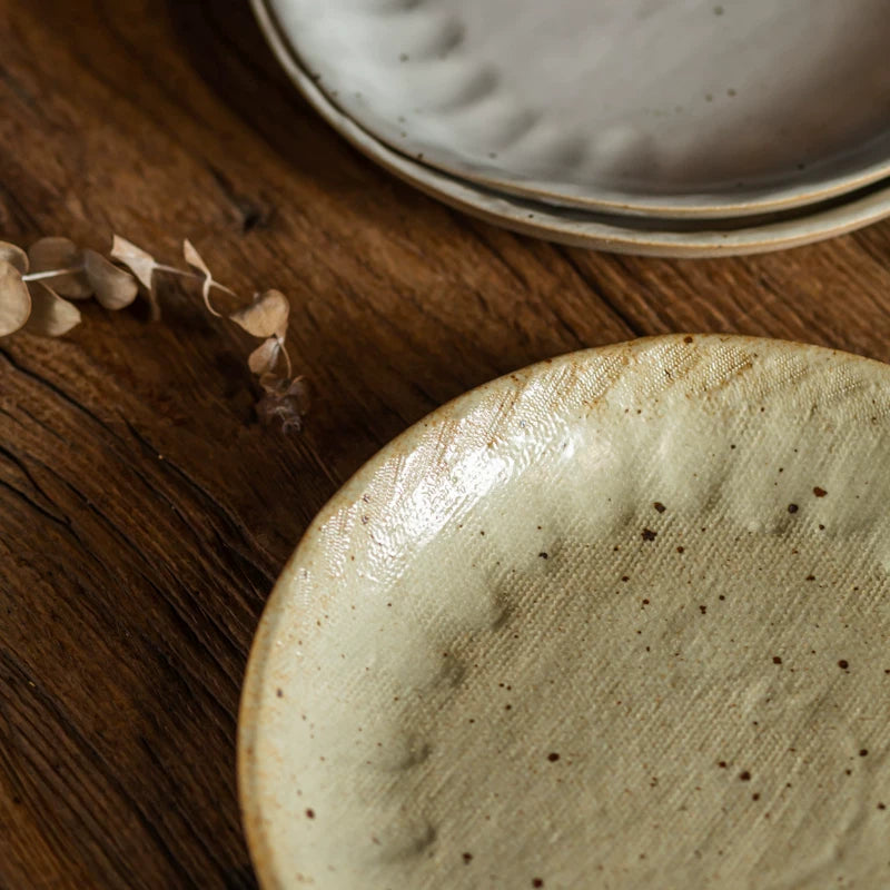 A close-up of a speckled, yellowish-beige ceramic plate with a slightly raised, uneven rim.