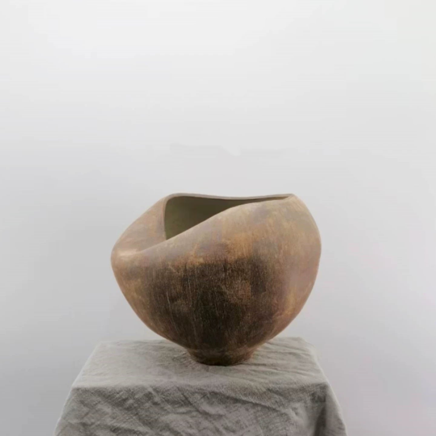 A handmade beige ceramic vase with a unique, sculptural folded design and a textured matte finish.
