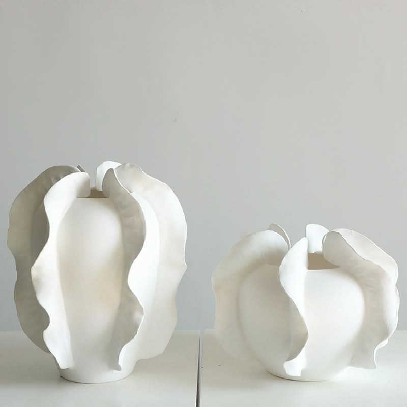 Modern white ruffled ceramic vase set with organic, sculptural forms on a white surface.