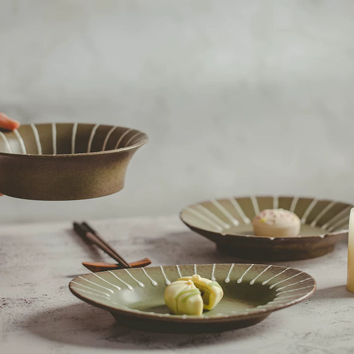 Table setting with two ceramic plates featuring green centers and white striped rims, holding pastries.