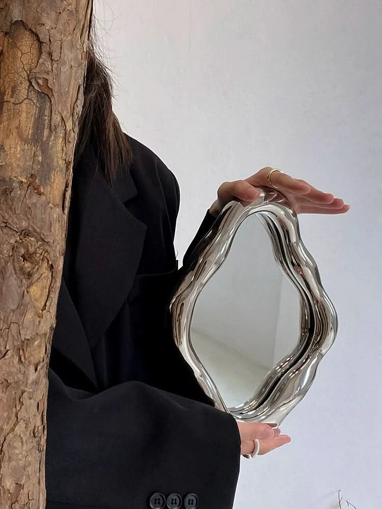 Modern abstract silver metal vanity mirror, handheld with organic shape.