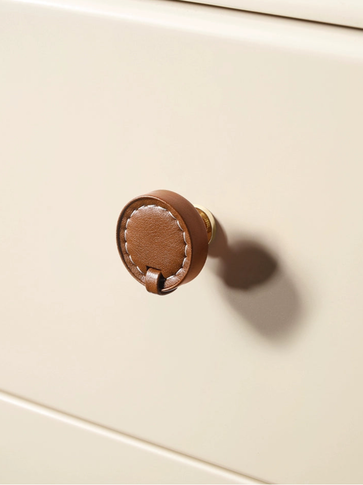Brown leather-wrapped drawer pull with white stitching on a cream cabinet. Modern farmhouse style.