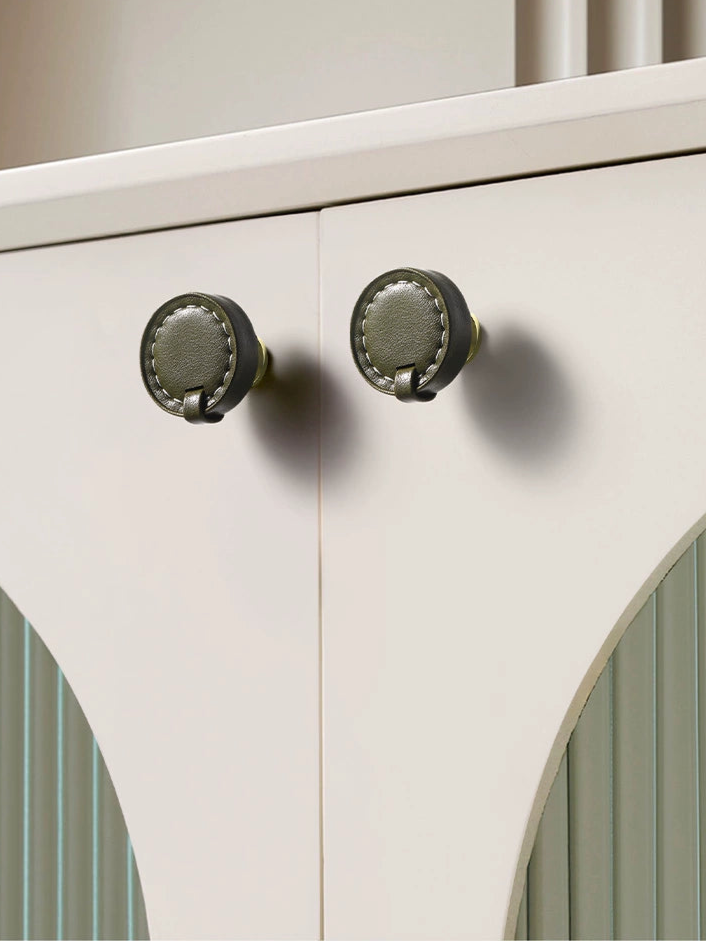 Olive green leather round drawer pulls & cabinet knobs with gold hardware on white cabinetry.