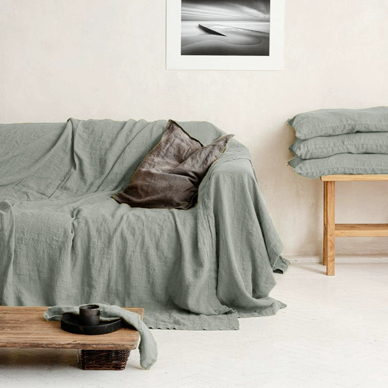 Mustard yellow linen sofa throw blanket draped over couch with one brown cushion.