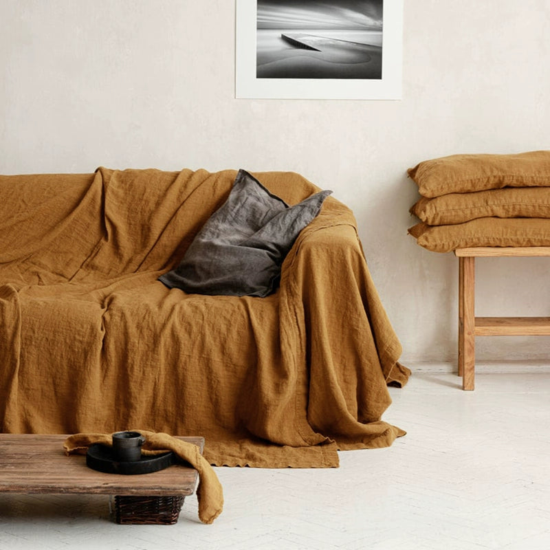Mustard Yellow Linen Sofa Throw Blanket draped over a couch, with gray pillow. Cozy living room decor.