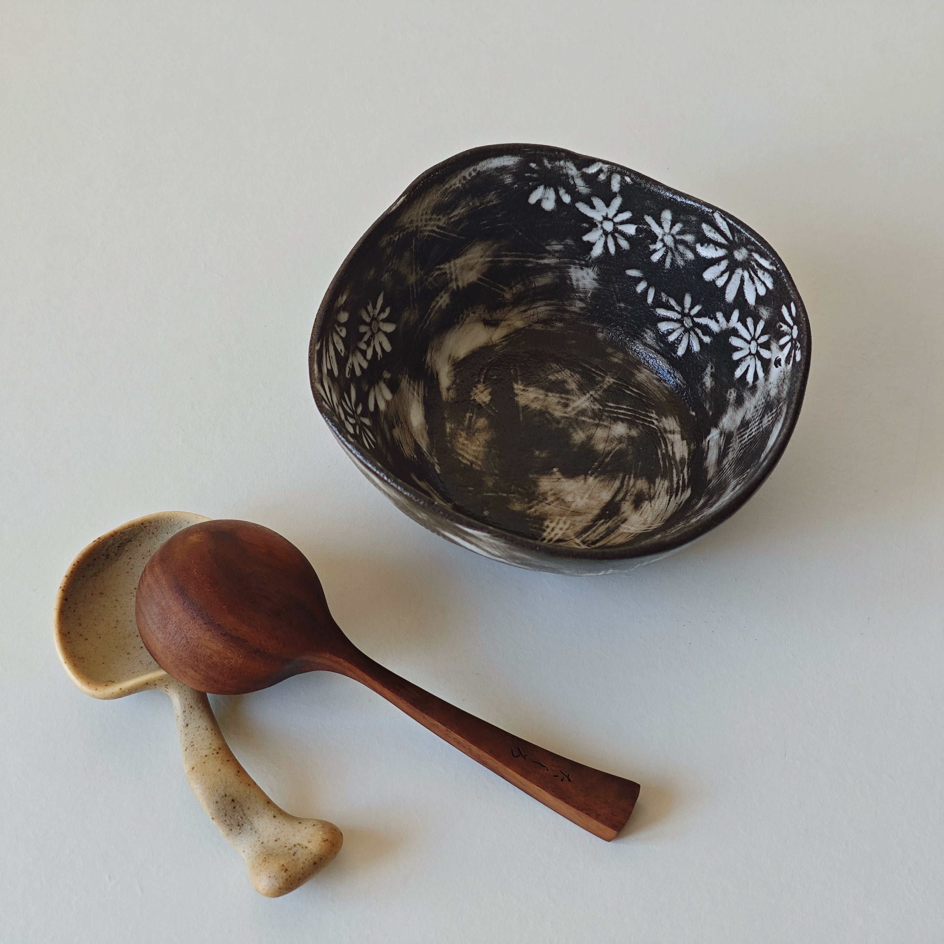 Hand-painted black and white floral ceramic bowl with wood and speckled ceramic spoons.