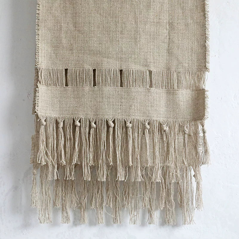 Beige linen table runner with tassels and rustic woven detail.