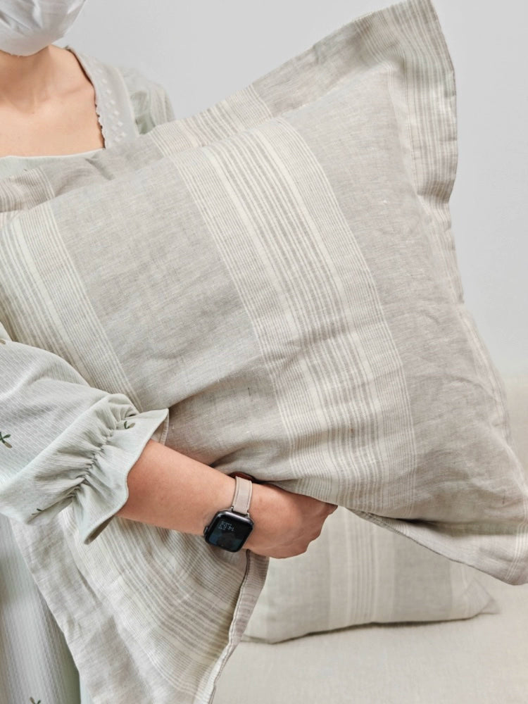 Gray striped linen pillow cover held by person in light gray clothing.
