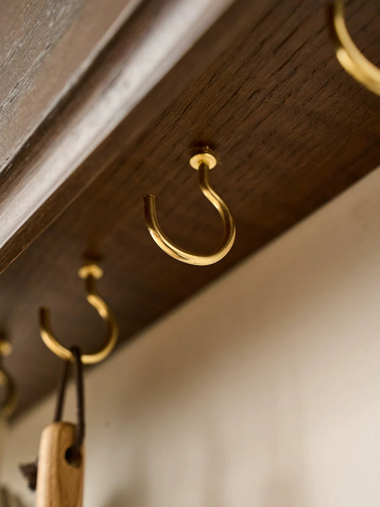 Detail of dark wood shelf with brass hooks holding leather straps and wooden tags.