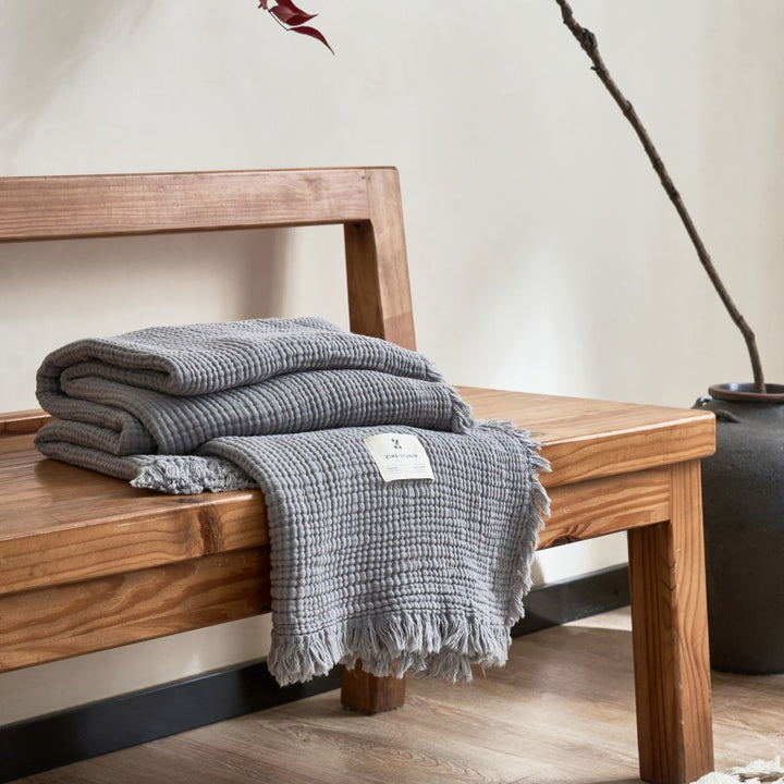 Gray textured throw blanket on wooden bench.