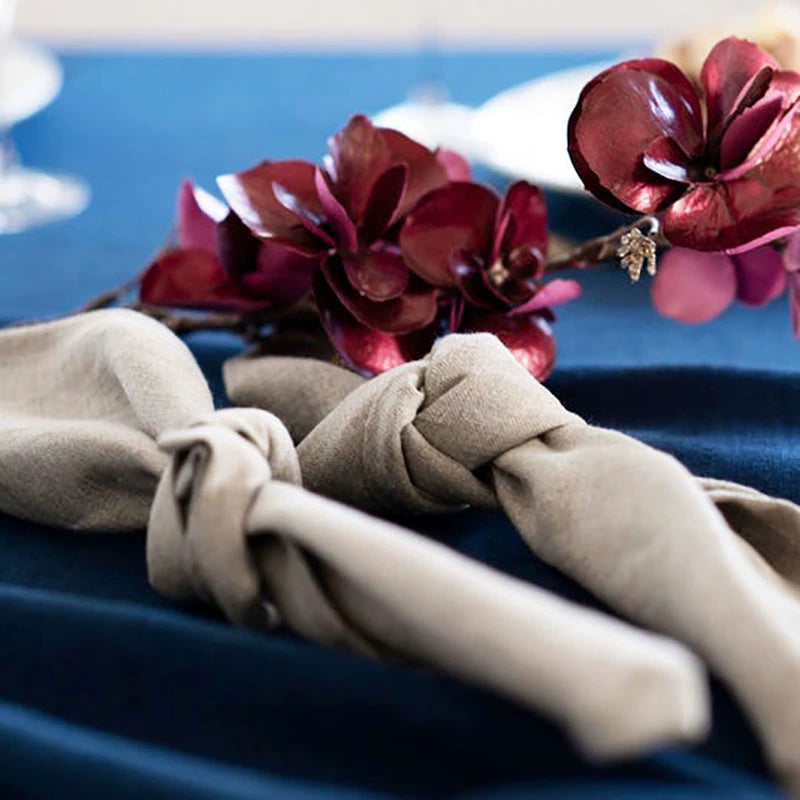 Elegant Linen Table Napkins (Set of 4) in beige, knotted and set on a navy blue tablecloth with burgundy flowers.