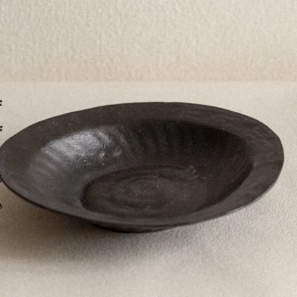 Wide, shallow ceramic bowl in matte black with an organic, uneven textured surface.