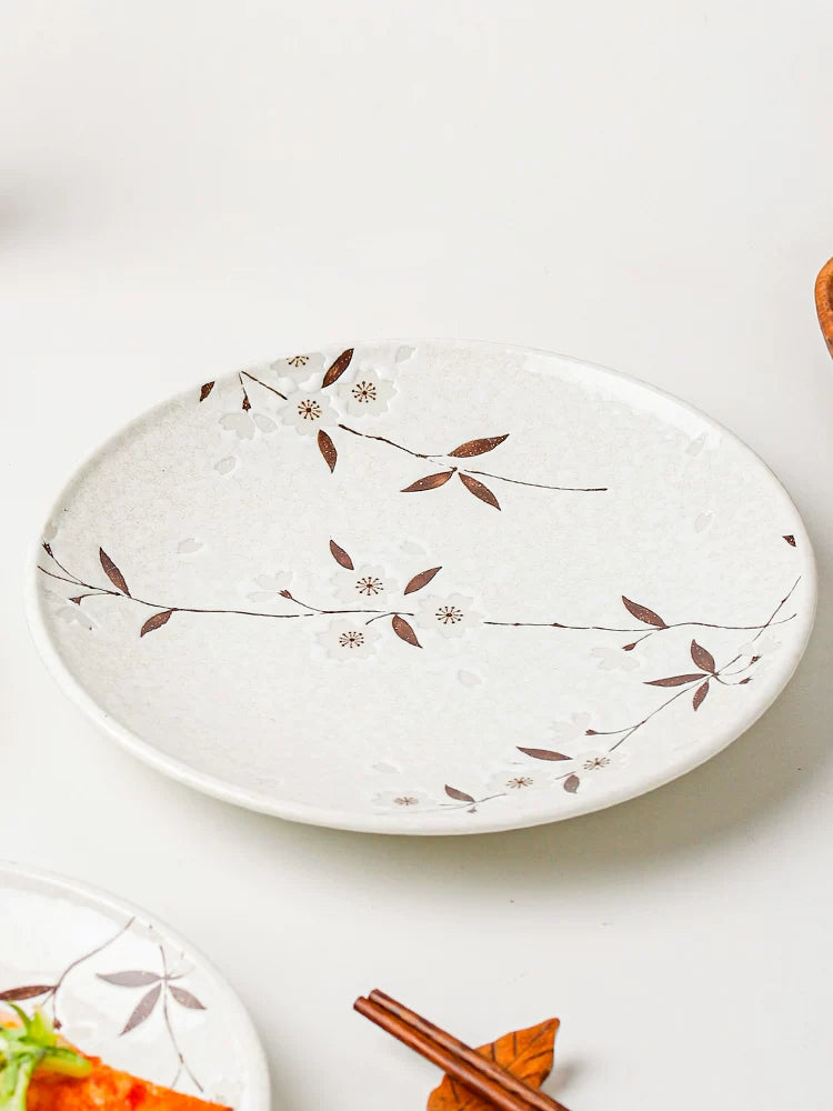 White ceramic oval serving plate with brown cherry blossom pattern, next to chopsticks and food.