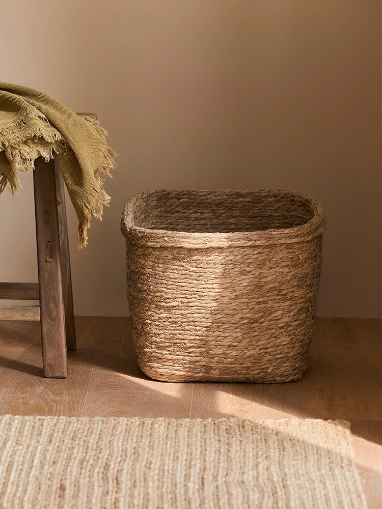 Natural rattan storage basket, square shape, with a throw draped on a wooden stool in a home setting.