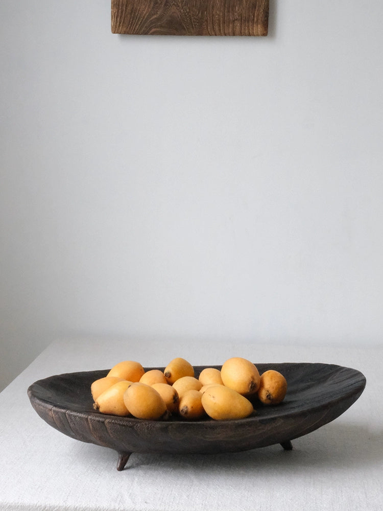 Dark brown wooden oval platter with fruit, likely mangosteen.