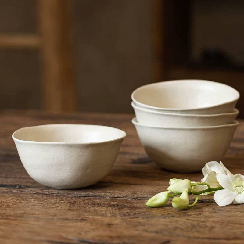 Stack of creamy white ceramic bowls and a single bowl next to white orchid flowers on a rustic wooden table.