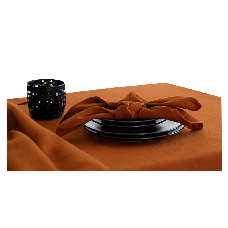 Elegant linen table napkins in rust, knotted on black plates, with a decorative lantern.