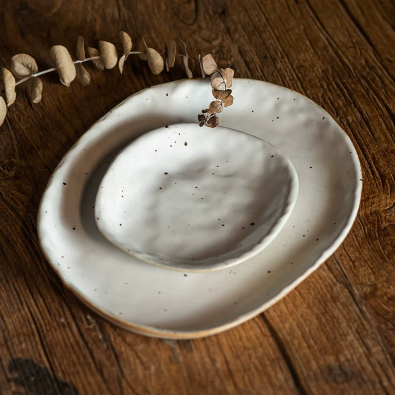 Two irregular, cream-colored ceramic plates with speckled glaze stacked on a rustic wooden table.