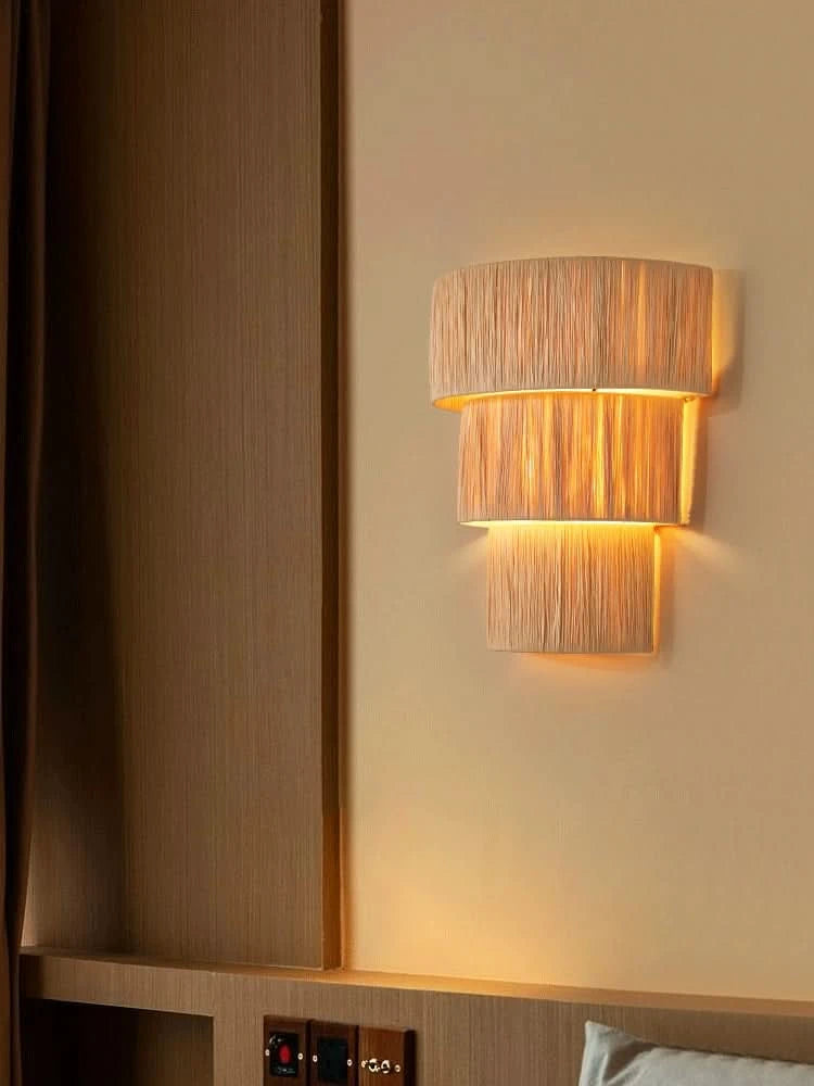 Natural raffia wall sconce light with three tiers, casting warm ambient light in a bedroom.