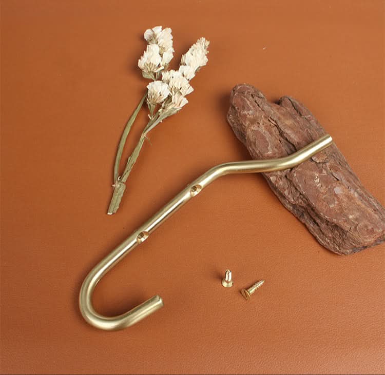 Minimalist brass wall hook with dried flowers and wood on brown surface.